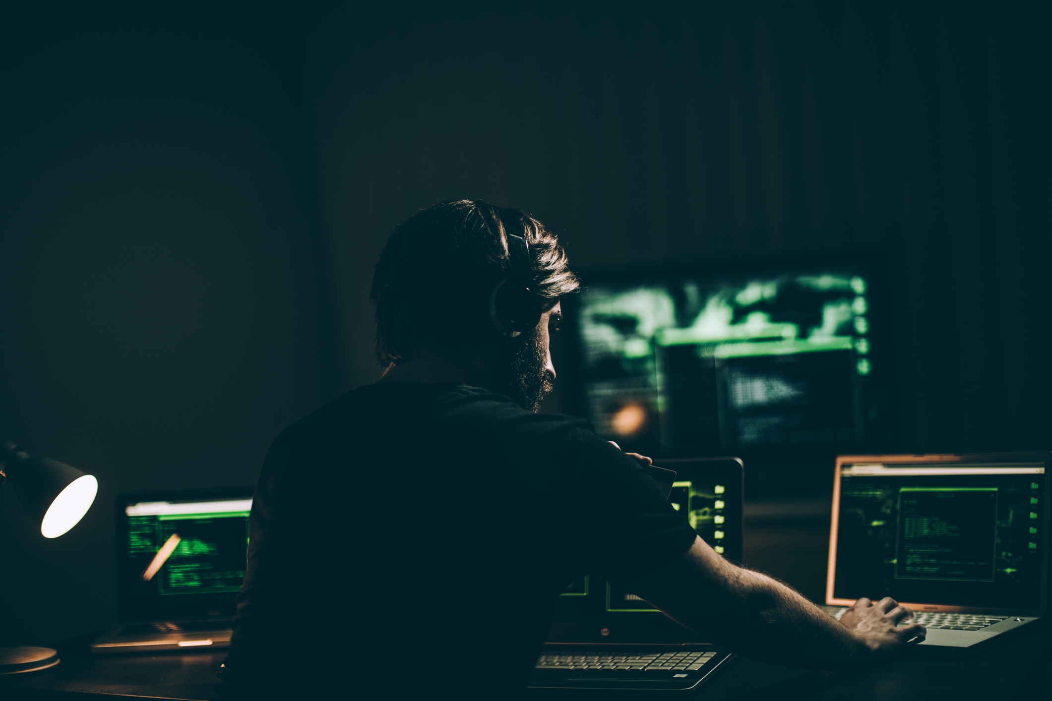 Computer hacker holding credit card while working on laptop late at night