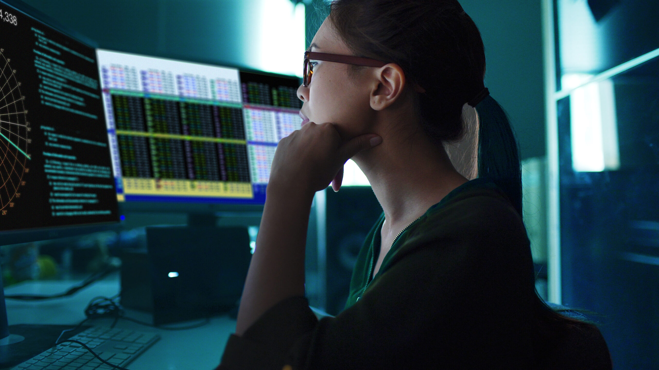 Stock photo of an Asian woman surrounded by computer monitors in a dark room